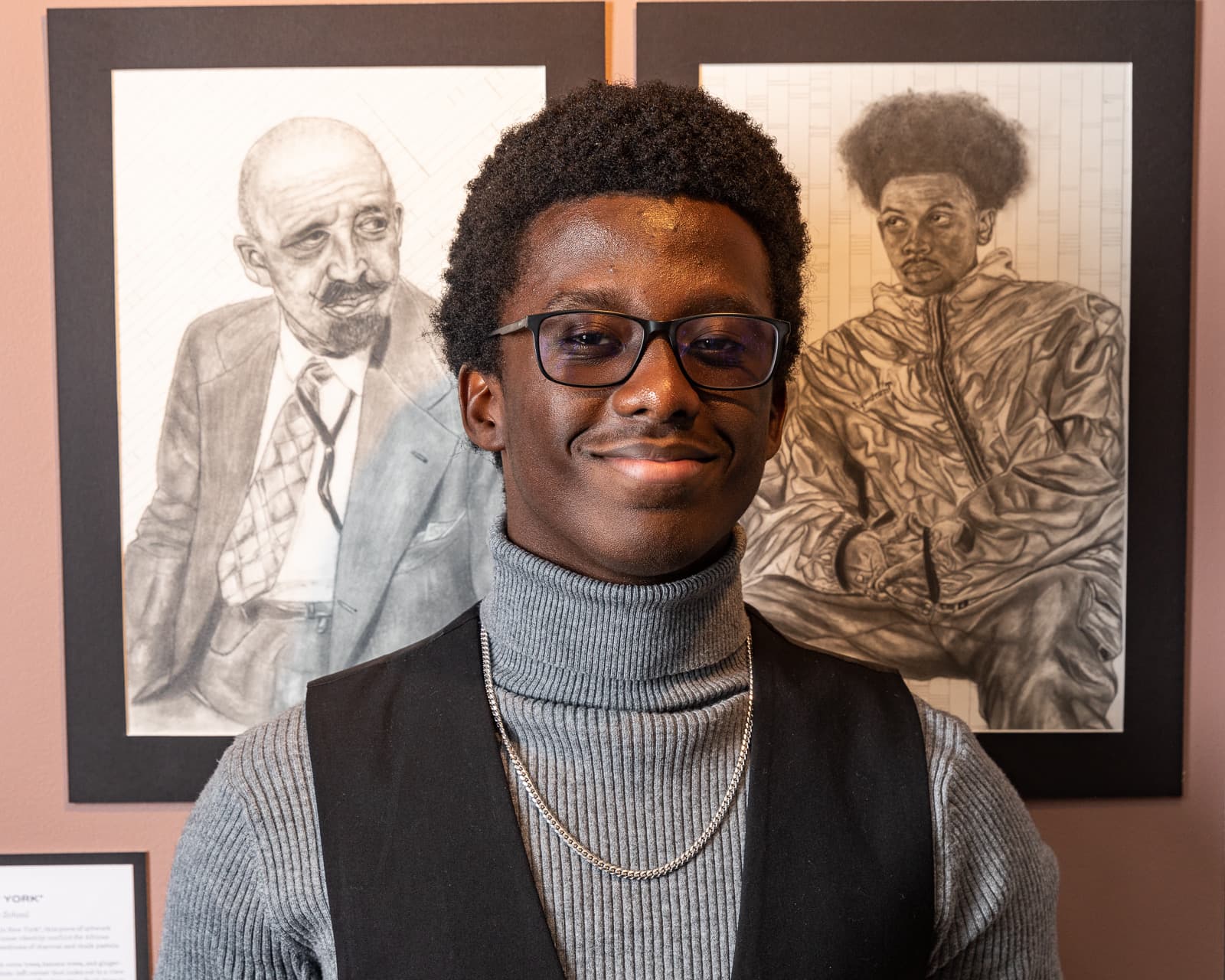 Allah-u-Abha standing beside his graphite portraits at an exhibition
