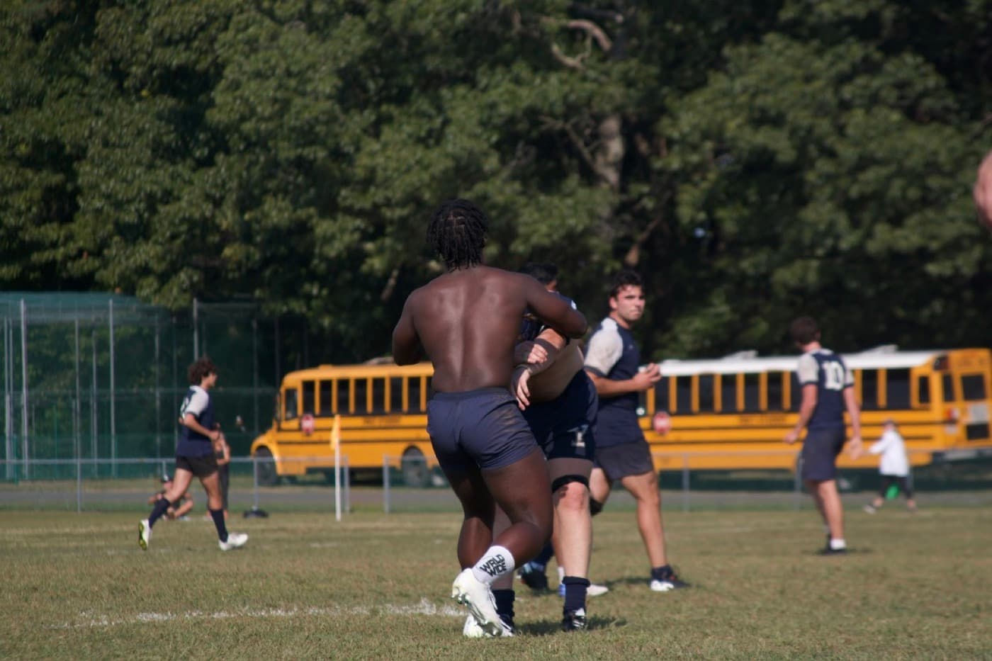 Rugby match in motion, carrying the ball past a yellow school bus