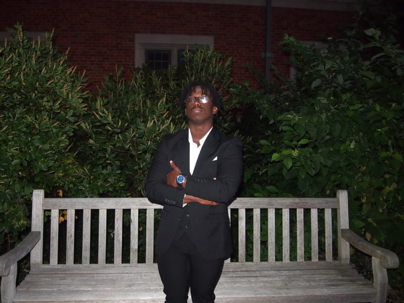 Allah-u-Abha in a black suit at night, arms crossed, on Yale's campus